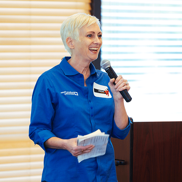 A middle aged employee wearing an Indiana State University shirt smiles while talking into a microphone during an Enrollment Management retreat for employees.